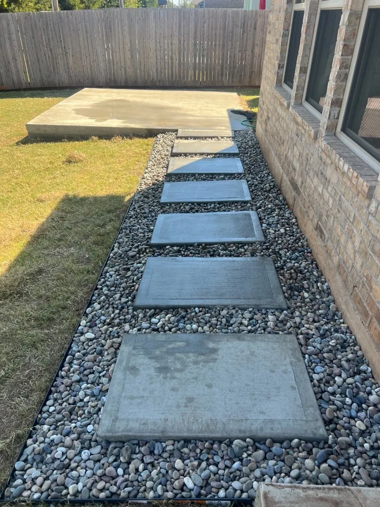 Broom-finish concrete pavers with picture-frame borders set in decorative river rock leading to a new concrete patio in Norman, OK