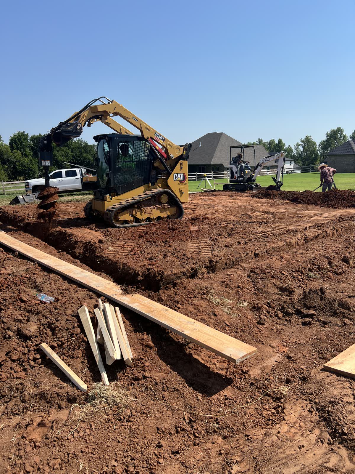 Excavation and site grading for pier foundation in Edmond, Oklahoma — skid steer and excavator working red clay lot